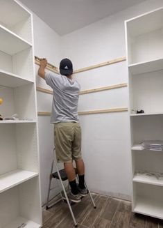 a man standing on a stepladder in front of white shelving shelves with wood planks