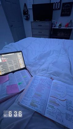 an open laptop computer sitting on top of a bed next to notebooks and papers