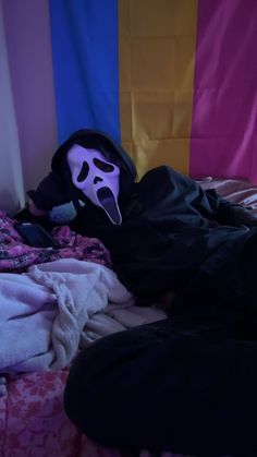 a person laying in bed with a mask on their face and wearing a black jacket