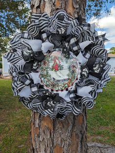 a wreath on the side of a tree with black and white ribbons hanging from it