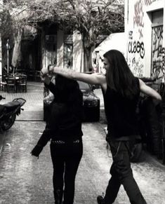 two people walking down a street with graffiti on the walls