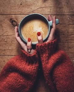 a woman holding a cup of coffee in her hands on top of a wooden table