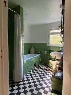 a bathroom with green and white tiles on the floor, tub and shower curtain are open