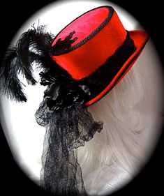 "This Gothic top hat is heavy red velvet wrapped with a black velvet and lace hatband and has a soft black crushed tulle bow & long tails in back. This Victorian style riding hat has black satin roses centered in the back. There is a silver antiqued Celtic cross centered on a beautiful black lace applique on the front of the crown. A black lace applique rests on the back of the crown's top. The brim & crown edge are trimmed in black satin braid. This hat is loaded with black curled ostri Gothic Fitted Brimmed Top Hat, Fitted Gothic Brimmed Top Hat, Fitted Red Halloween Hat, Red Fitted Hat For Costume, Red Fitted Vintage Top Hat, Red Fitted Mini Hat For Costume Party, Vintage Red Hats For Costume Party, Vintage Red Hat For Costume Party, Fitted Top Hat For Kentucky Derby Costume