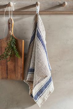 two towels are hanging on a rack next to a cutting board with a sprig of rosemary