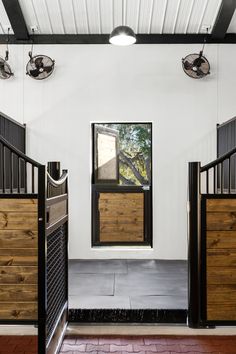 the inside of a horse stable with wooden stalls and doors leading to an open area