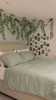 a bed with green sheets and pillows next to a plant on the wall above it