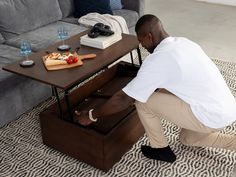 a man kneeling on the floor in front of a coffee table with drawers underneath it