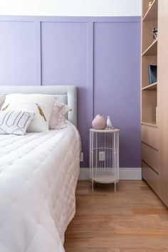 a white bed sitting in a bedroom next to a book shelf and purple painted walls