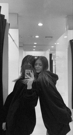 two women standing in front of a mirror taking a selfie