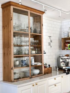 a wooden cabinet filled with lots of dishes and glasses on top of a kitchen counter