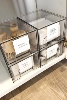 three clear boxes with labels on them sitting on a shelf next to other items in the room