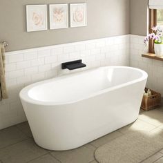 a white bath tub sitting in a bathroom next to a sink and window with pictures on the wall