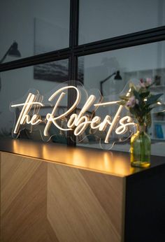 the sign is lit up in front of a window with flowers on it and lights behind it