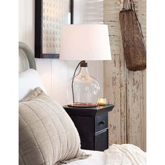 a lamp on a night stand next to a bed with pillows and a basket hanging from the wall