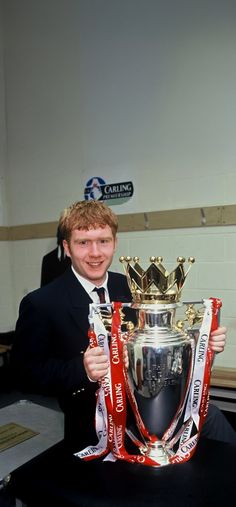 a man in a suit and tie holding up a silver trophy with red ribbon around it