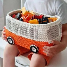 a small child holding a basket filled with toy cars and trucks on it's lap