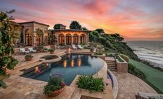 an outdoor swimming pool next to a large house with a view of the ocean at sunset