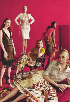 the models are posing in front of red walls and colorful furniture, with one woman sitting on a chair