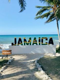 a sign that reads jamaica on the side of a road next to the ocean and palm trees