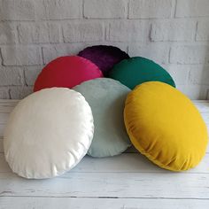 four different colored pillows sitting on top of a white wooden floor next to a brick wall