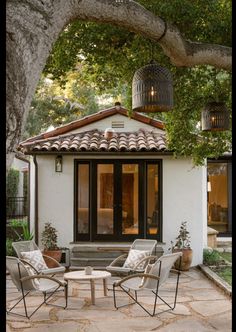 an outdoor patio with chairs and tables under a tree in front of a house,