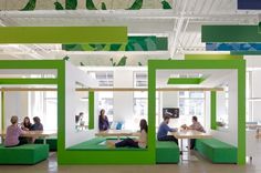 people are sitting at tables in an office with green and white booths on the walls