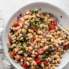 a white bowl filled with bean salad and garnished with parsley on the side