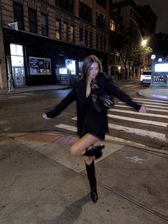 a woman is dancing on the sidewalk in front of a crosswalk at night time