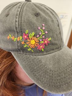 a woman wearing a gray hat with embroidered flowers on the front and side of it