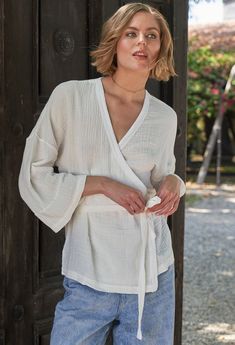 Eco friendly caftans and tunics inspired by the ocean, made on main street. Ethically sourced and locally made in Los Angeles. Our super soft, easy-care cotton gauze fabric gets a glamorous upgrade in our flattering kimono sleeve wrap top. With a self belt, this one allows you to choose your look. Tie it loose for an elegant drapy top or wrap it around your waist to accentuate your shape. The relaxed kimono sleeves are just the right bracelet length and can be easily folded back for a more dramatic look. Pairs perfectly with our gauze palazzo pant and just about everything else in your wardrobe. Sheerness: none Model height: 5'10" Fabric: 100% Cotton Machine wash, tumble, hang or lay flat to dry. // Flowy Cover-up With Kimono Sleeves For Loungewear, Chic V-neck Wrap Top For Beach, Luxury White Wrap Kimono, Summer Cover-up With Relaxed Fit And Kimono Sleeves, Flowy V-neck Kimono, Kimono Wrap Top, White Kimono, Cotton Gauze Fabric, Kimono Wrap