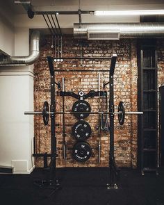 an empty gym room with barbells and weight plates on the wall, in front of a brick wall