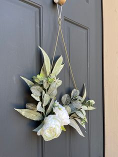 a wreath hanging on the front door with white flowers and greenery attached to it