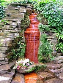 a red fire hydrant sitting in the middle of a lush green garden next to a stone wall