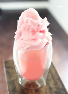 there is a pink ice cream in a glass cup on the wooden table and it looks like something out of space