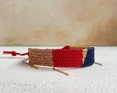 This red and navy blue coloured boho and hippie style bracelet is comfortable to wear and lightweight around the wrist with adjustable sliding knot closure so fits most sizes both women, men and children. It harmonizes with every outfit, every occasion, also perfect as a gift. Lac plated stainless steel chain in gold colour added for modern design. Woven length 14cm, extension braided length 9cm, width 1.2cm Designed and made in a smoke free - pet free environment.  All our products are nickel f Red Adjustable Cord Bracelet For Festival, Red Adjustable Cord Bracelet For Festivals, Red Woven Bracelets For Festival, Red Woven Bracelet For The Beach, Red Woven Bracelet For Beach, Red Band Bracelet As Gift, Adjustable Red Band Bracelets, Red Band Bracelet For Gift, Red Woven Beach Bracelets