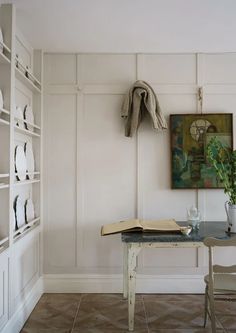 a table with a book and vase on it in front of a white painted wall