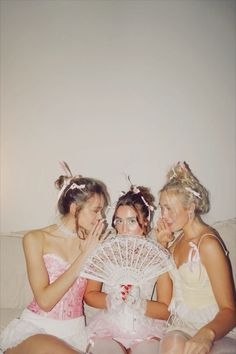 three women sitting on a couch with one holding a fan in front of her face