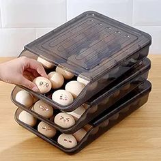 three plastic containers filled with wooden buttons on top of a table next to a person's hand