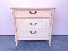 a white wooden dresser with two drawers and black knobs on the bottom drawer, in front of a pink wall