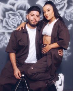 a man and woman sitting next to each other in front of a wall with roses on it