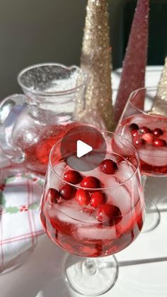 two glasses filled with red liquid and cranberries on top of a white table