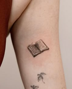 a woman's arm with an open book and flying birds tattoo on her left side