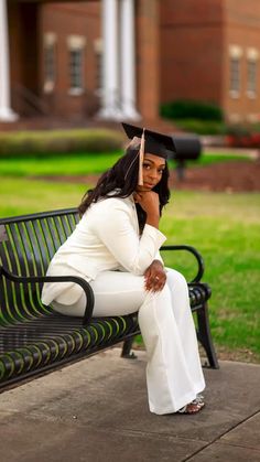 a woman sitting on top of a black bench wearing a graduation cap and white pants