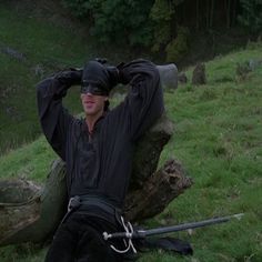 a man sitting on top of a lush green field next to a fallen tree trunk