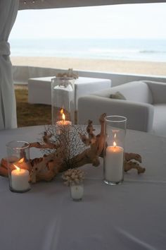 two candles are sitting on a table next to some glass vases and driftwood