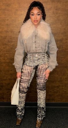 a woman standing in front of a wooden wall wearing high heels and a fur collar