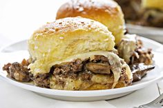 a close up of a plate of food with meat and cheese on it, next to a roll