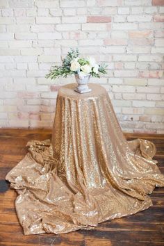 a gold sequin table cloth with white flowers on it in front of a brick wall