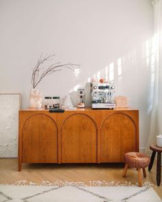 a room with a table, chair and coffee maker on top of the cabinet in front of it